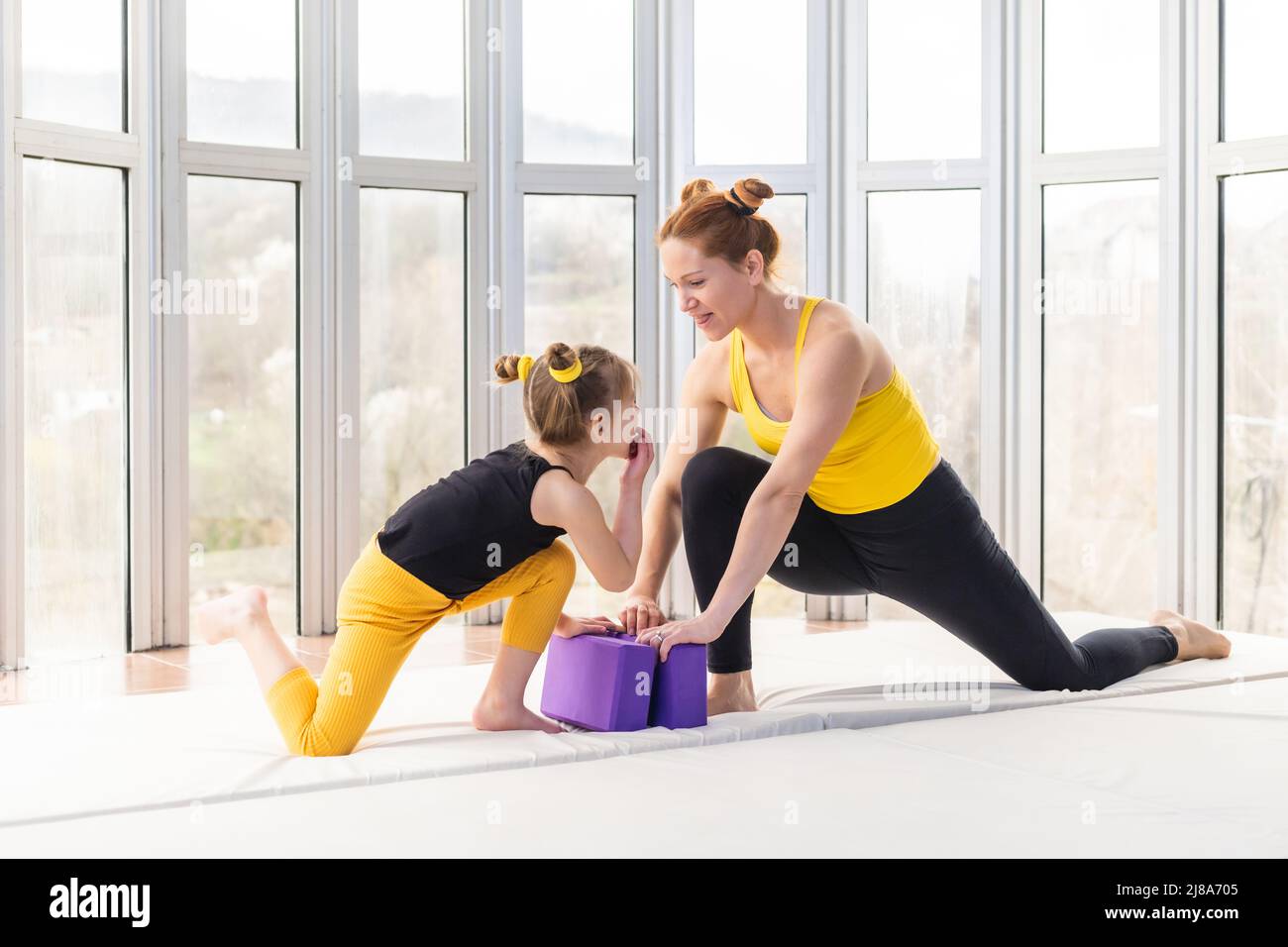 Giovane madre in forma che sta giocando con la sua figlia prima di pratica di yoga Foto Stock