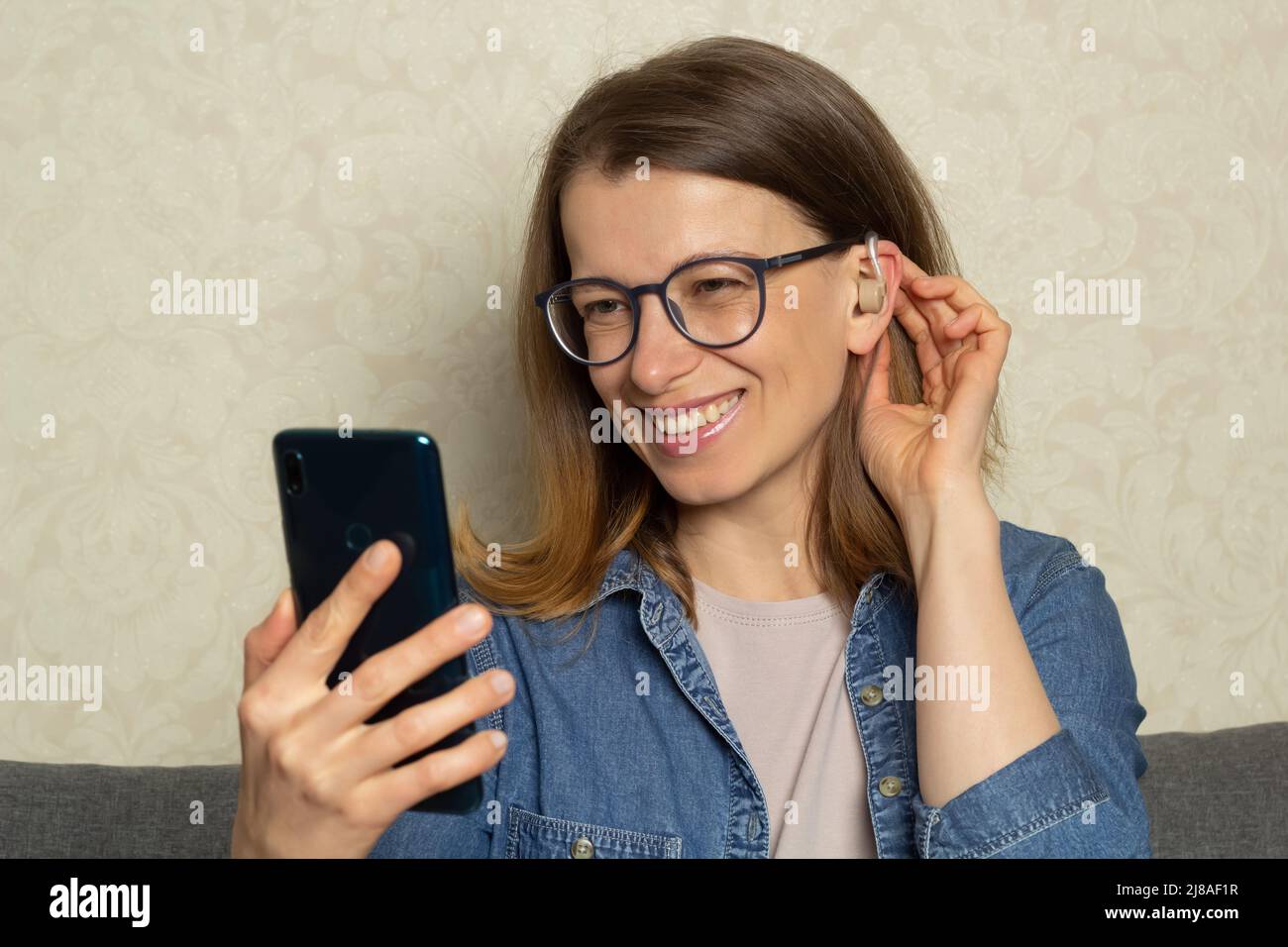 Una donna sta parlando al telefono utilizzando un apparecchio acustico sull'orecchio per amplificare il suono. Foto Stock