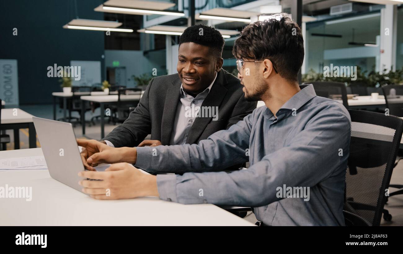 L'analista finanziario dell'uomo arabo spiega la strategia di affari l'imprenditore africano che punta sul laptop che discute l'avvio che esamina i benefici del contratto di progetto Foto Stock