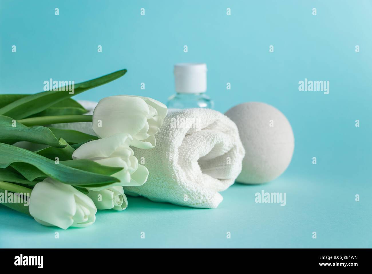 Prodotti per la cura della pelle su sfondo blu. Cosmetici naturali e tulipani bianchi. Posiziona per il testo. Foto Stock