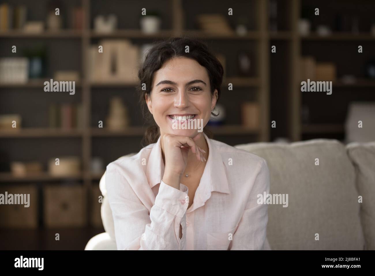 La donna sorride fissando la macchina fotografica e rilassandosi sul divano di casa Foto Stock