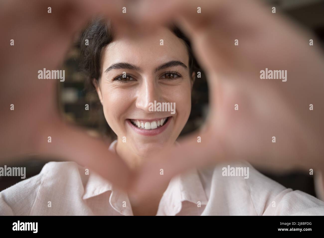 Closeup donna fissando la fotocamera attraverso le dita unite che mostrano l'amore Foto Stock