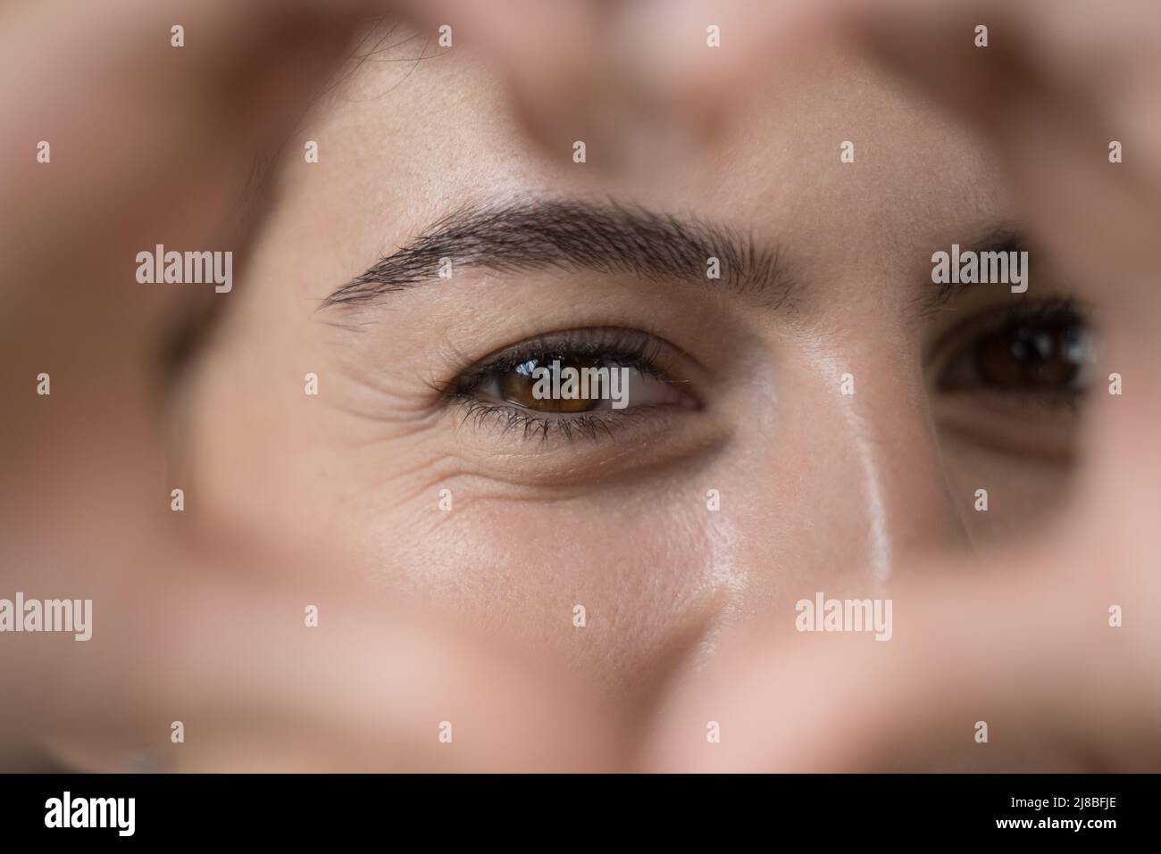 Giovane donna che unisce le dita mostrando a macchina fotografica simbolo di amore Foto Stock