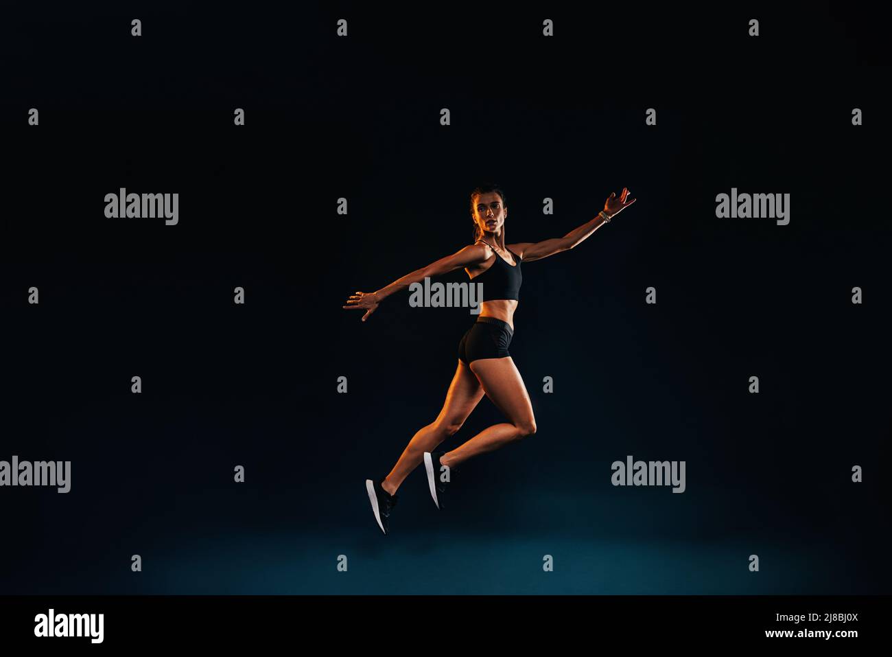Donna sottile che lavora su sfondo nero. Atleta femminile che fa salti in studio. Foto Stock