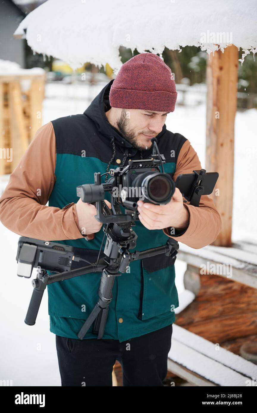 Uomo videografo che realizza filmati, utilizzando una fotocamera montata su un'attrezzatura stabilizzatore in inverno. Foto Stock