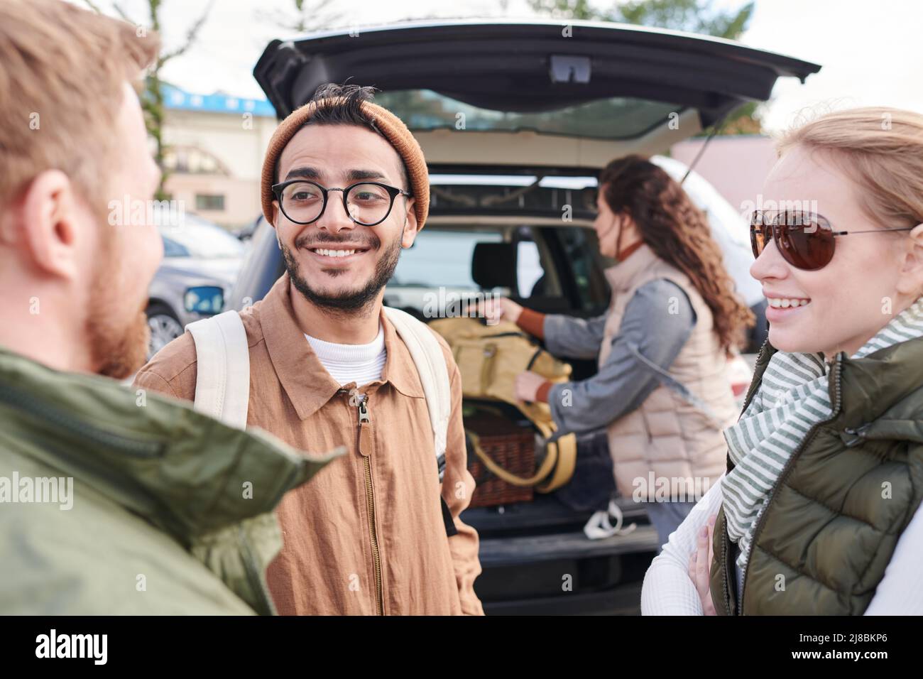 Gruppo di giovani positivi multi-etnico pianificazione viaggio percorso mentre ragazza imballaggio bagagli in tronco auto in background Foto Stock