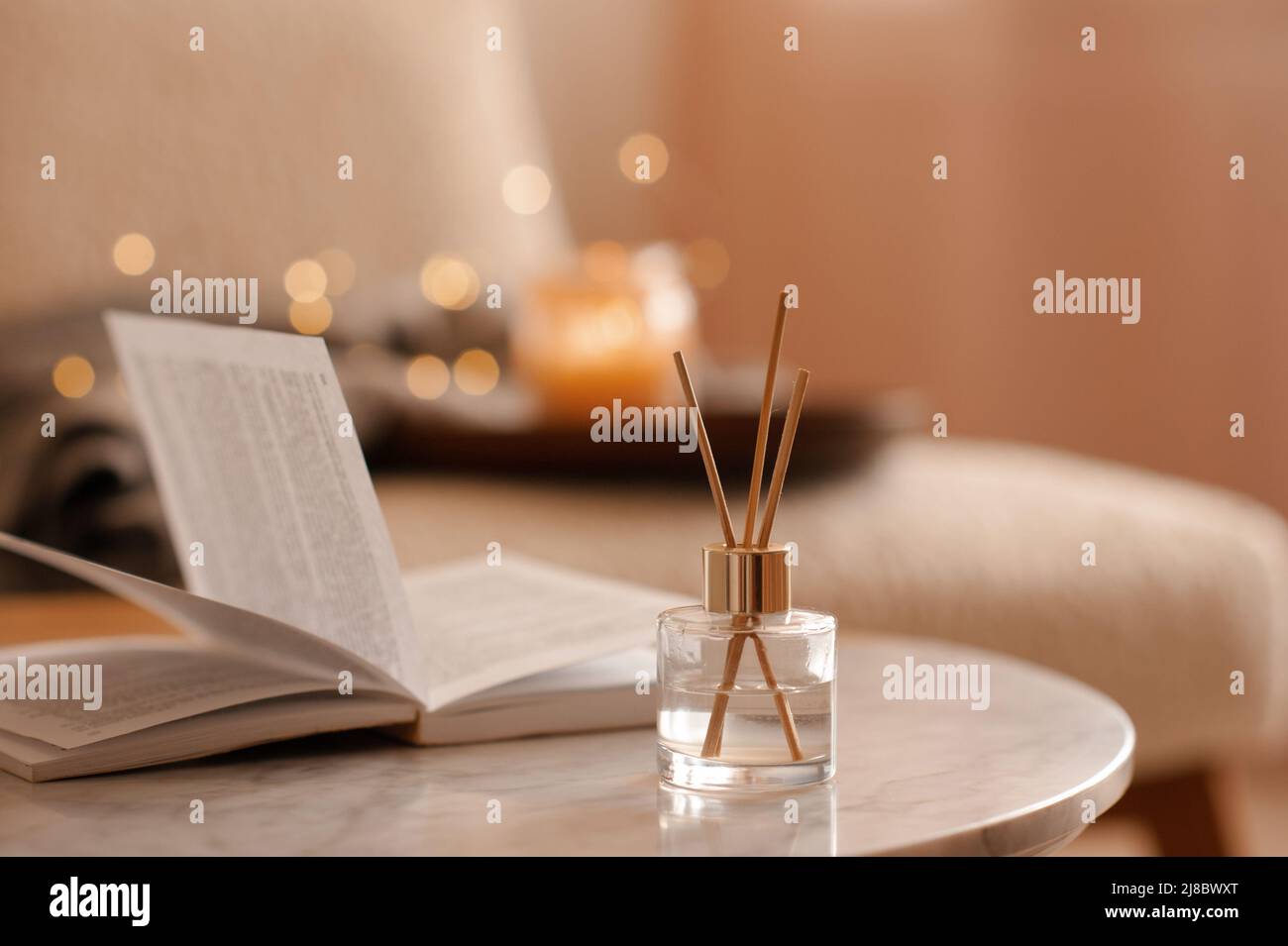 Fragranza domestica liquida in diffusore con libro di carta aperto sul tavolino in camera da letto all'interno primo piano sopra candela profumata. Atmosfera accogliente e igge. Aro Foto Stock
