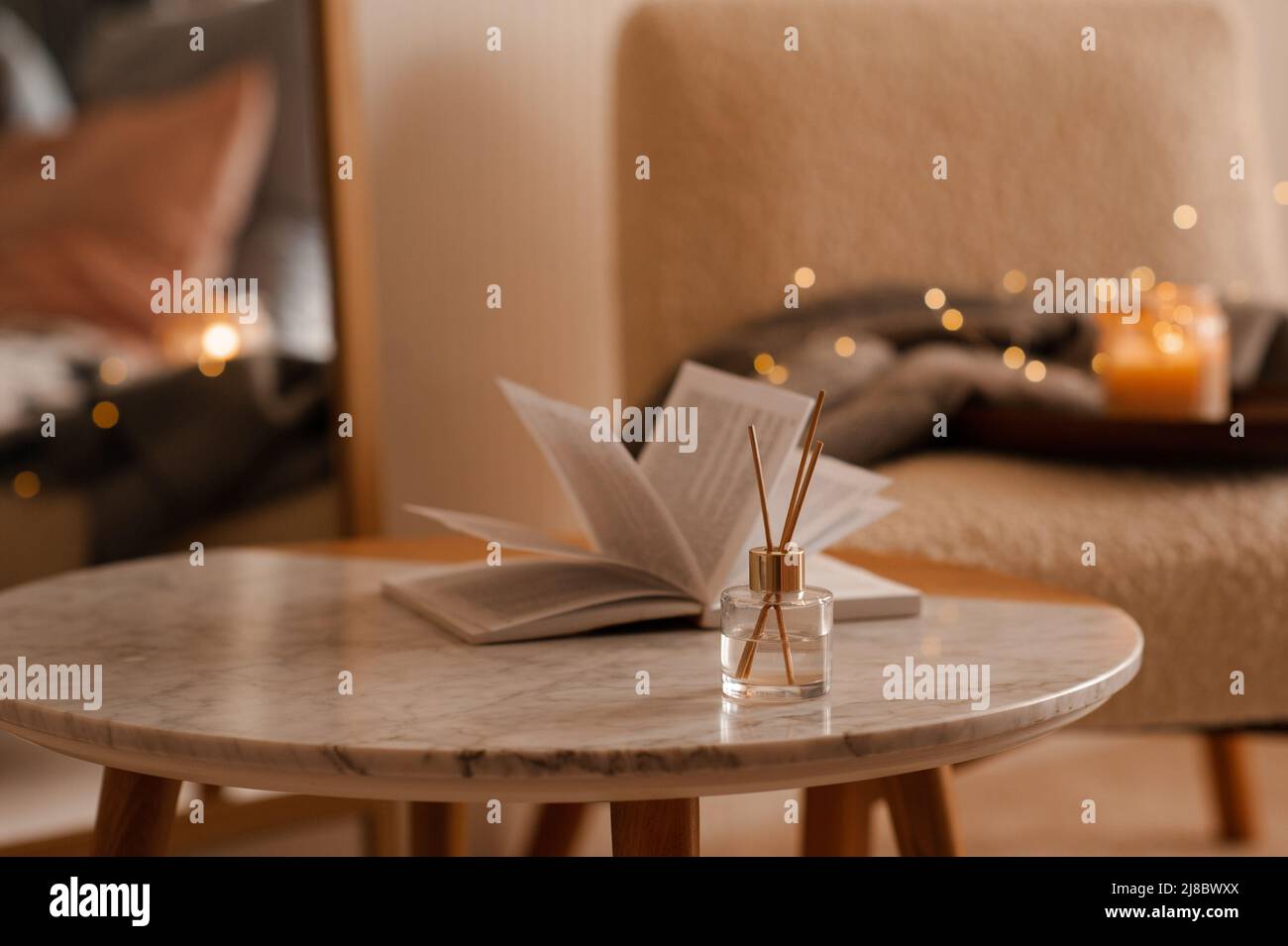 Fragranza domestica liquida in diffusore con libro di carta aperto sul tavolino in camera da letto all'interno primo piano sopra candela profumata. Atmosfera accogliente e igge. Aro Foto Stock