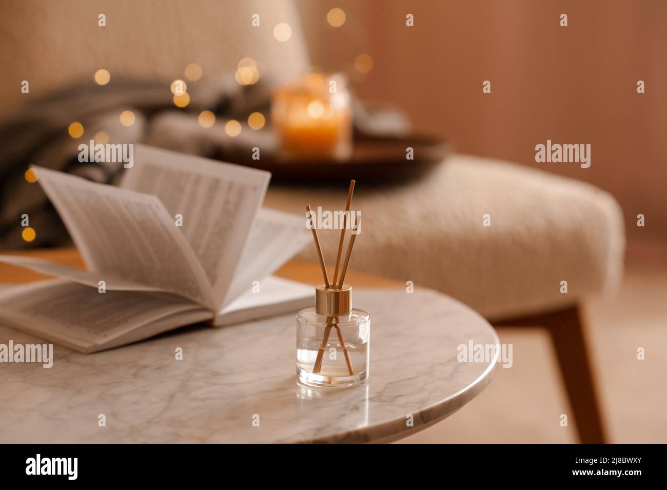 Fragranza domestica liquida in diffusore con libro di carta aperto sul tavolino in camera da letto all'interno primo piano sopra candela profumata. Atmosfera accogliente e igge. Aro Foto Stock