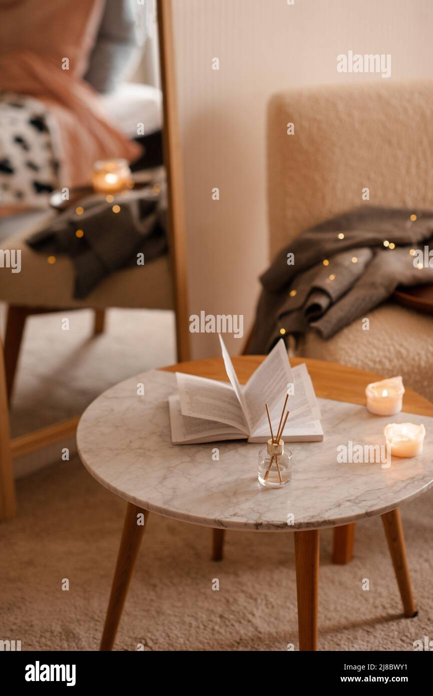 Fragranza domestica liquida in diffusore con libro di carta aperto sul tavolino in camera da letto all'interno primo piano sopra candela profumata. Atmosfera accogliente e igge. Aro Foto Stock