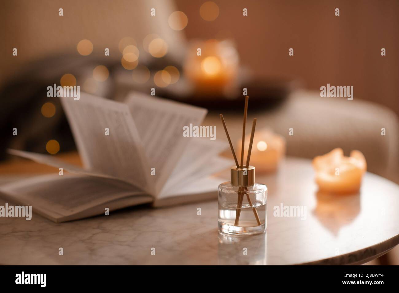 Fragranza domestica liquida in diffusore con libro di carta aperto sul tavolino in camera da letto all'interno primo piano sopra candela profumata. Atmosfera accogliente e igge. Aro Foto Stock