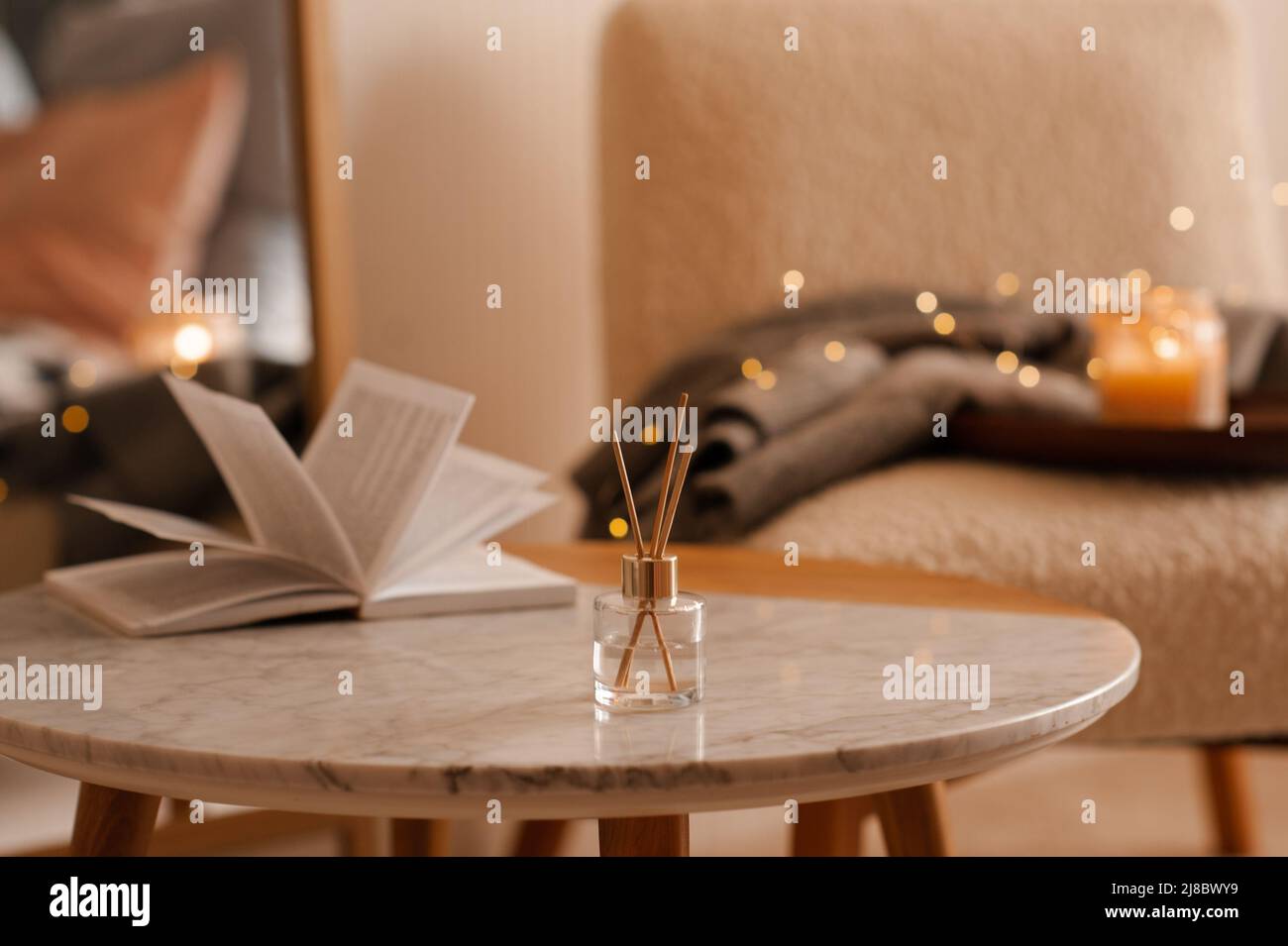 Fragranza domestica liquida in diffusore con libro di carta aperto sul tavolino in camera da letto all'interno primo piano sopra candela profumata. Atmosfera accogliente e igge. Aro Foto Stock