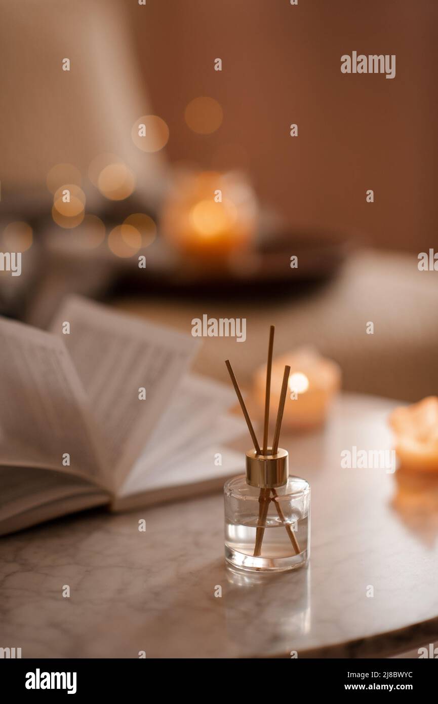 Fragranza domestica liquida in diffusore con libro di carta aperto sul tavolino in camera da letto all'interno primo piano sopra candela profumata. Atmosfera accogliente e igge. Aro Foto Stock