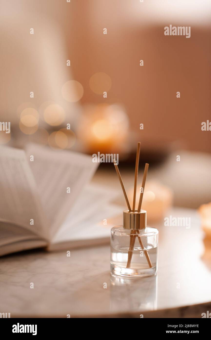 Fragranza domestica liquida in diffusore con libro di carta aperto sul tavolino in camera da letto all'interno primo piano sopra candela profumata. Atmosfera accogliente e igge. Aro Foto Stock