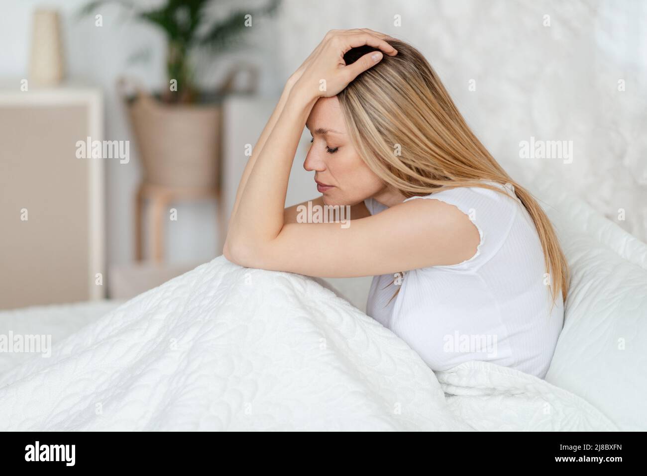 Disperazione infelice giovane bionda europea femmina che soffre di insonnia e mal di testa seduta a letto Foto Stock