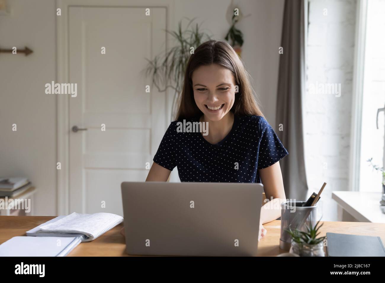 Felice studentessa seduta a casa tavolo da lavoro con computer portatile Foto Stock