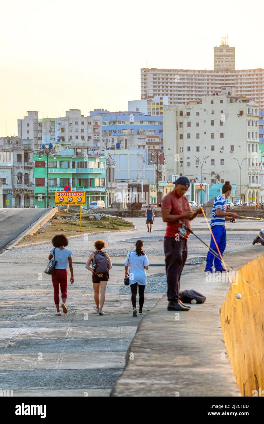 La gente cubana che pesca a El Malecon. Stanno usando le canne da pesca mentre sulla parte superiore della parete di mare. Lo skyline o il paesaggio urbano della capitale è visto in t Foto Stock