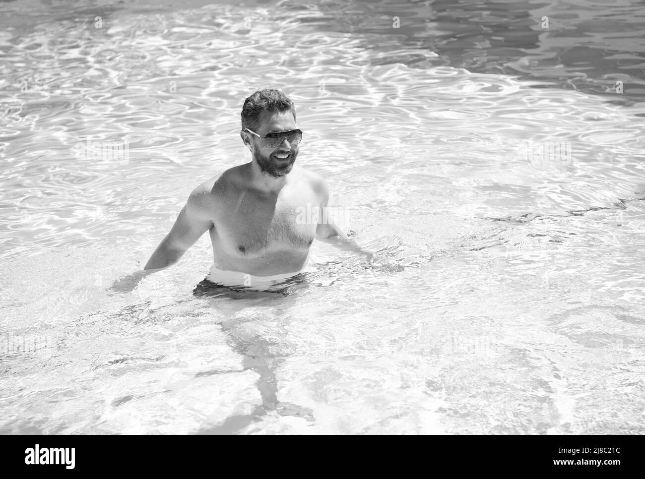 felice uomo bearded in occhiali da sole che nuotano in acqua di piscina durante le vacanze estive, estate Foto Stock