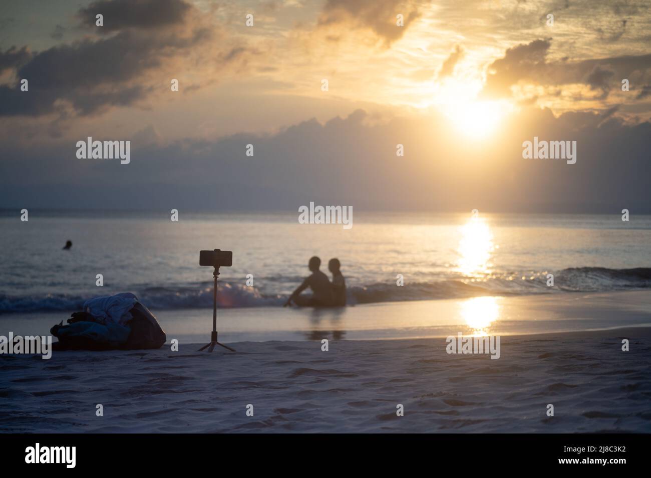 Coppia seduta sulla spiaggia con telefono su treppiede scattando foto che mostrano nomadi digitali, influencer e viaggiatori professionali nell'isola delle andamane in India Foto Stock