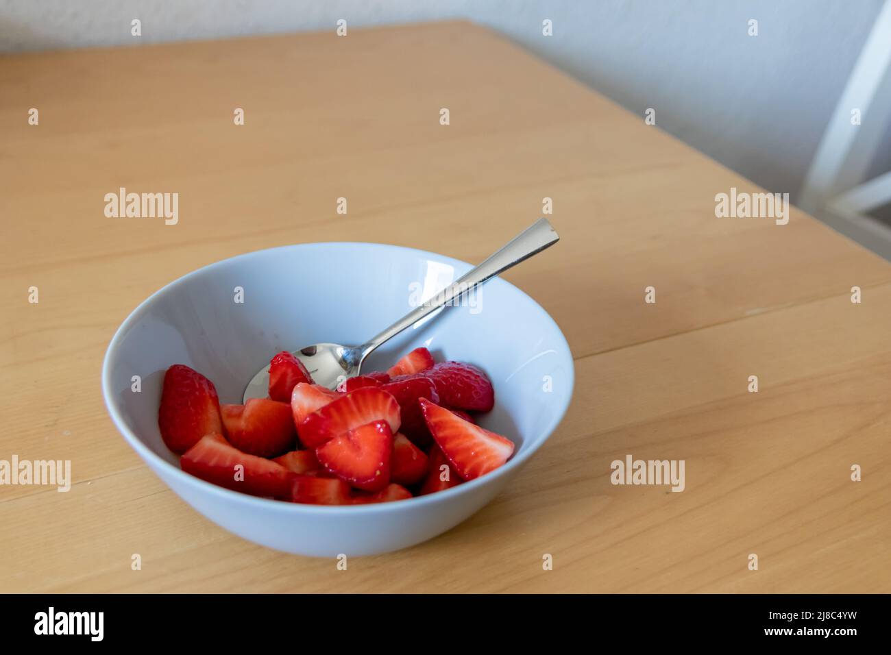 Molte fragole tagliate in ciotola sono pronte da mangiare con cucchiaio d'argento o come delizioso dito e snack sano con frutta rossa e vitamine su legno Foto Stock