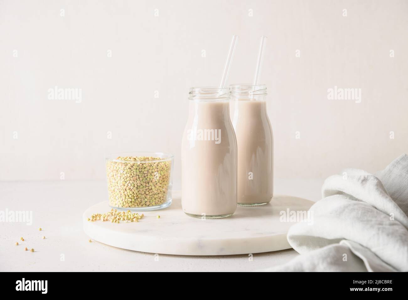 Latte di grano saraceno verde di cereali vegani in bottiglie sul piano della cucina bianco. Primo piano. Prodotto di sostituzione del latte a base di piante e privo di lattosio. Foto Stock