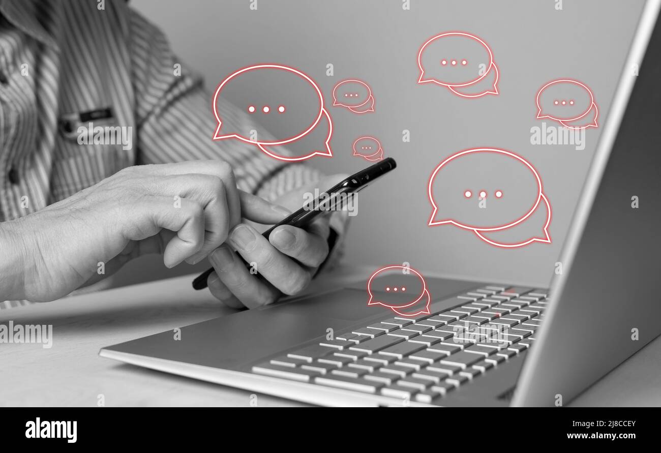 Uomo che utilizza il telefono per rispondere a commenti e recensioni negativi, commenti negativi, reclami dei clienti e reclami. Uomo seduto a tavola con computer portatile. Bianco e nero. Foto di alta qualità Foto Stock