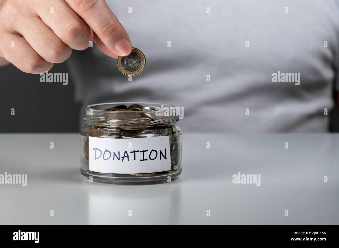 mettere a mano il penny in un vasetto di monete. Monete in vaso di vetro con etichetta di donazione su tavola di legno. Vista croppata dell'uomo che mette la moneta in un vaso di penny con il don Foto Stock