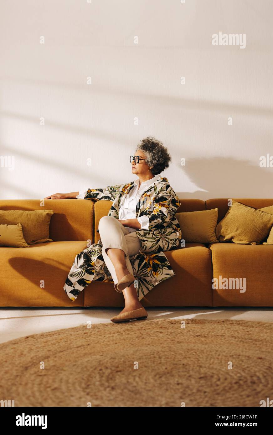 Donna d'affari anziana che guarda via con attenzione mentre si siede su un divano in una lobby d'ufficio. Donna d'affari contemplativa che lavora in un collaboratore creativo Foto Stock
