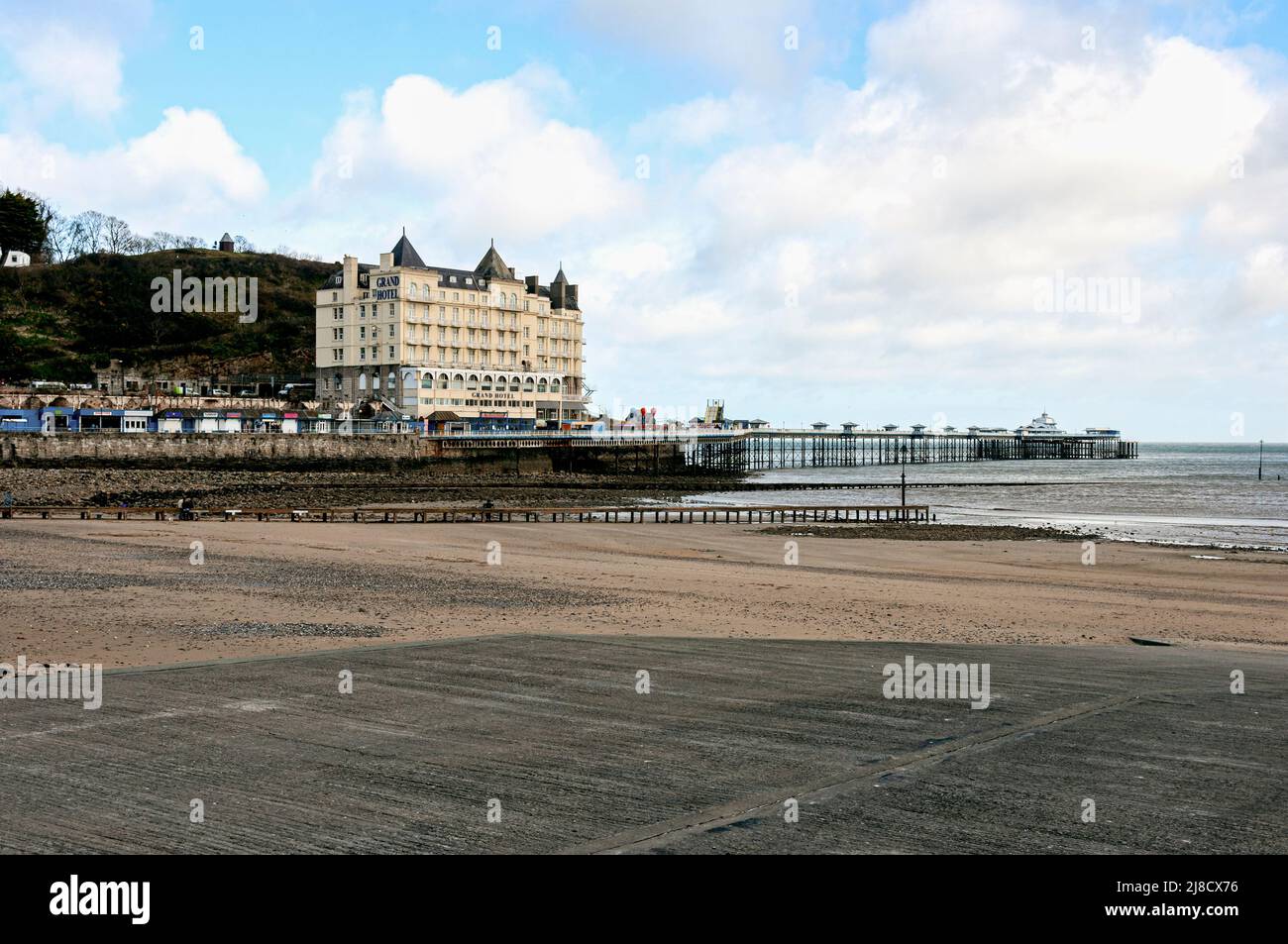 Un hotel e negozi si trovano su un altopiano roccioso accanto alla scogliera del Grande Orme ma sopra il molo che si estende sopra i ciottoli e la sabbia fino al mare Foto Stock