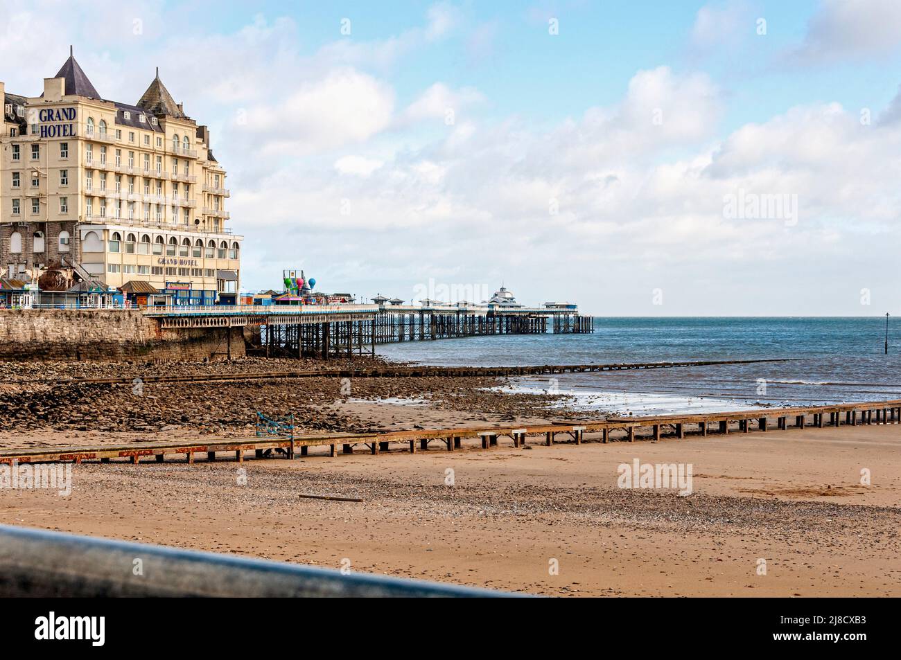 Un hotel e negozi si trovano su un altopiano roccioso accanto alla scogliera del Grande Orme ma sopra il molo che si estende sopra i ciottoli e la sabbia fino al mare Foto Stock