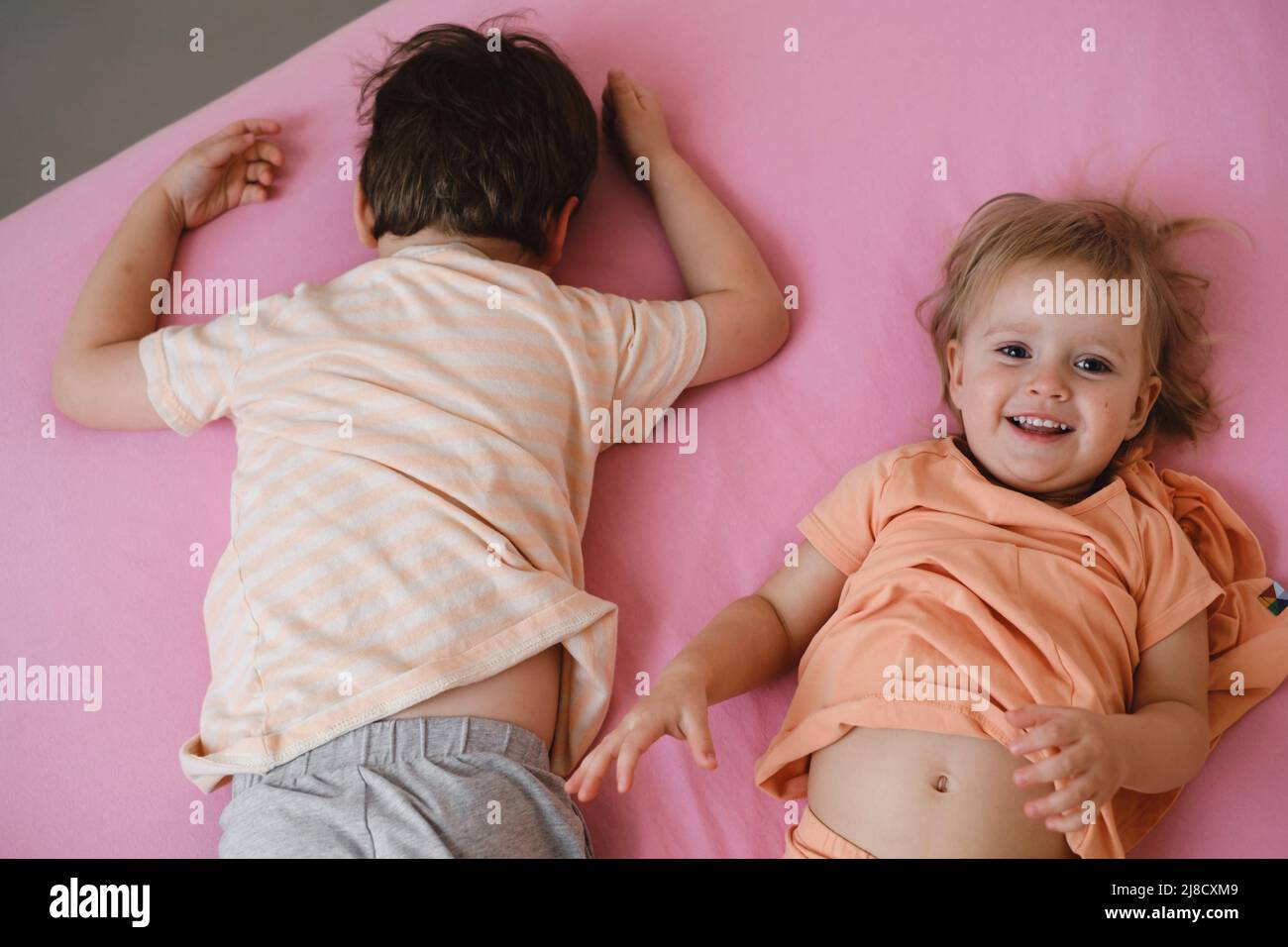 i bambini giocano sul letto colorato al mattino nascondono e cercano. Il bambino felice si trova sul letto rosa. Sorella e fratello in camera da letto, vista dall'alto, spazio copia. Bambino Foto Stock