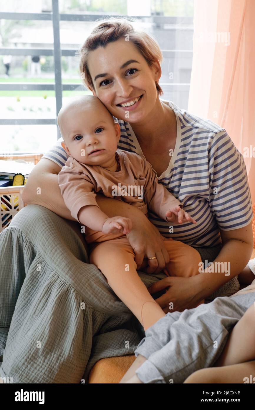 Madre con bambino nella camera dei bambini sopra la finestra. Ritratto di mamma e bambino a casa. Moderna famiglia. Bella mamma abbraccia neonato Foto Stock