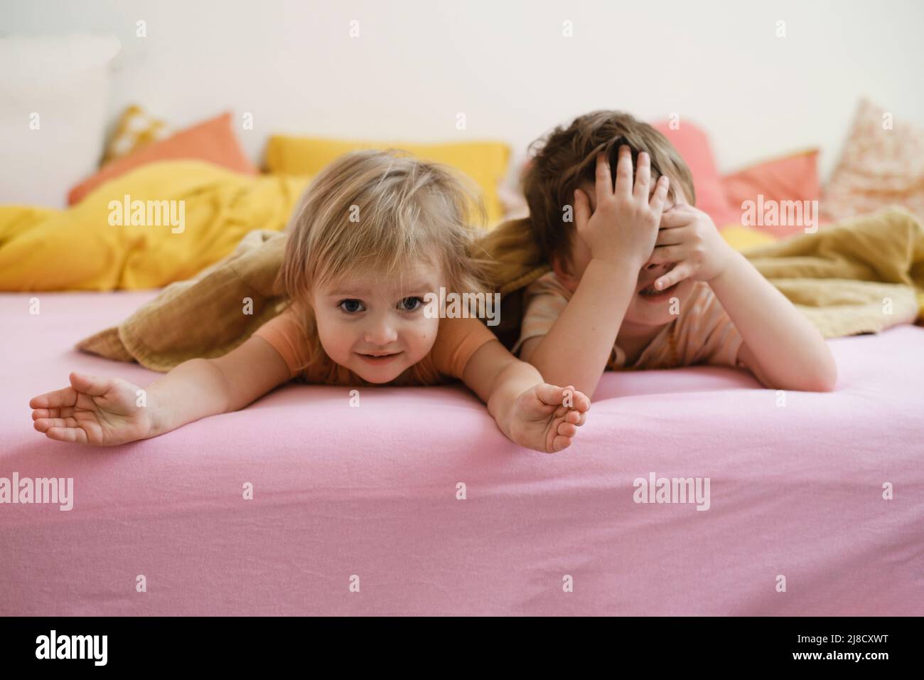i bambini giocano sul letto colorato al mattino nascondono e cercano. Il bambino felice si trova sul letto rosa. Sorella e fratello in camera da letto, spazio copia. Fratelli piccoli Foto Stock
