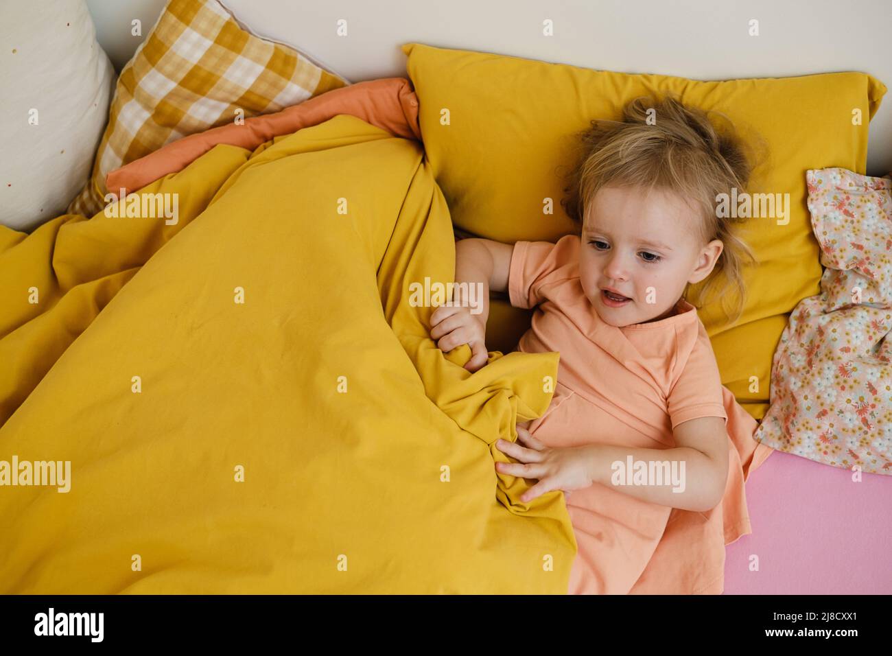 i bambini giocano sul letto colorato al mattino nascondono e cercano. Il bambino felice si trova sul letto rosa. Sorella e fratello in camera da letto, vista dall'alto, spazio copia. Bambino Foto Stock