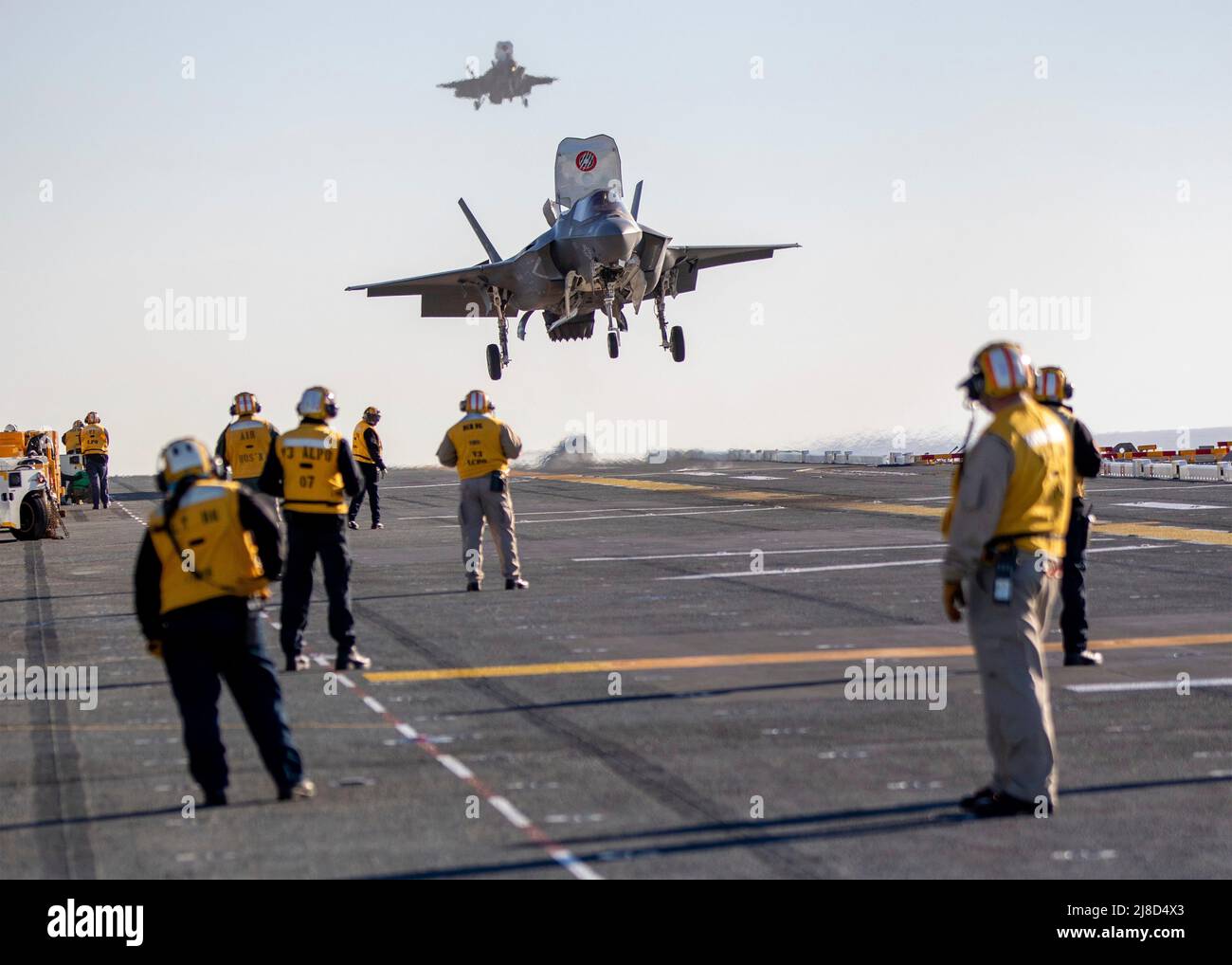 Gli equipaggi del ponte di volo della Marina degli Stati Uniti osservano come un aereo da caccia del corpo marino F-35B Lightning II, attaccato ai lethernecks volanti dell'attacco del combattente marino Squadron 122, effettua un atterraggio verticale sul ponte di volo della nave d'assalto anfibio di classe Wasp USS Makin Island, febbraio 2, 2022 operare sull'Oceano Pacifico. Foto Stock