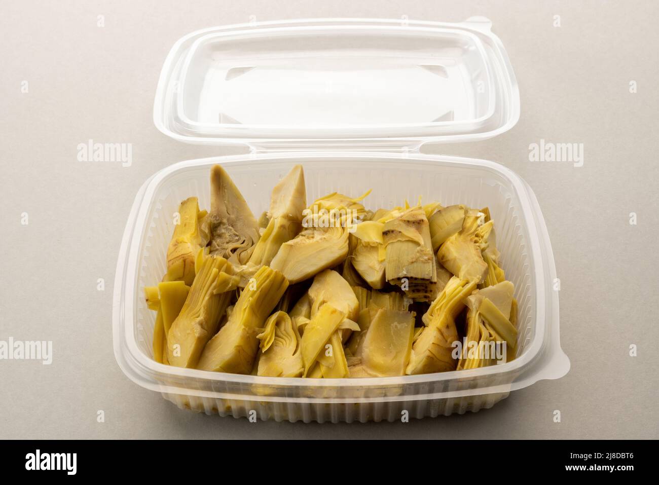 Zeppe di carciofi bolliti in scatola trasparente di plastica alimentare per refrigerazione o conservazione, su sfondo grigio chiaro Foto Stock