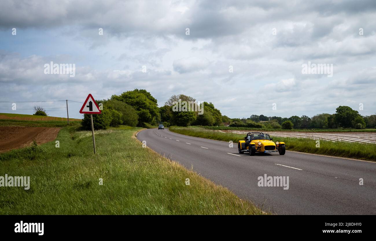 Una macchina sportiva gialla Caterham 7 (Lotus 7) guida in una giornata di sole lungo la campagna inglese A272 strada. Foto Stock