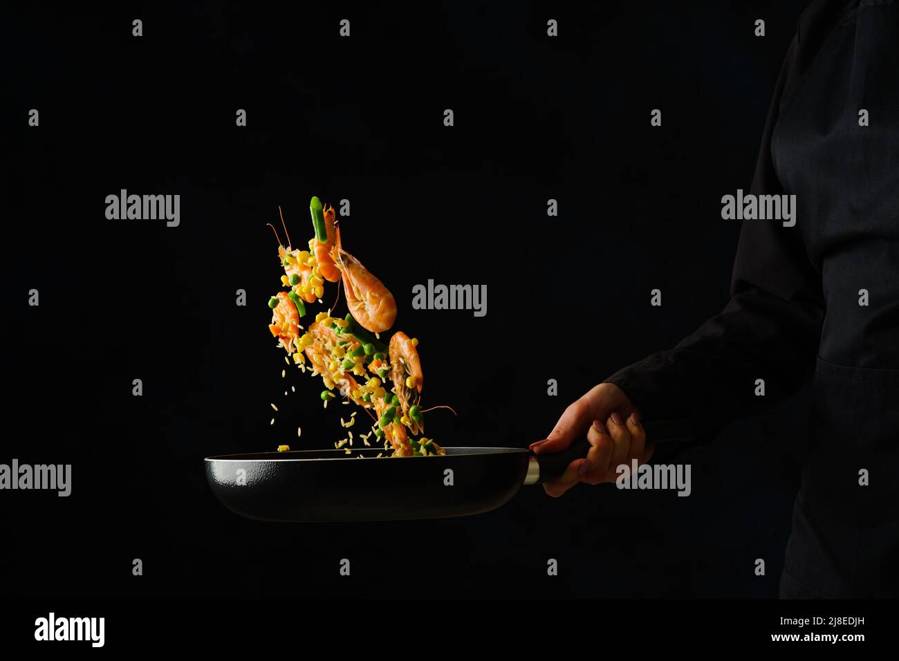 Lo chef cuoce il riso con i gamberi in una padella su sfondo nero. Levitazione. Ricette di frutti di mare, preparazione di frutti di mare. Libro di ricette, blog di cibo. Foto Stock