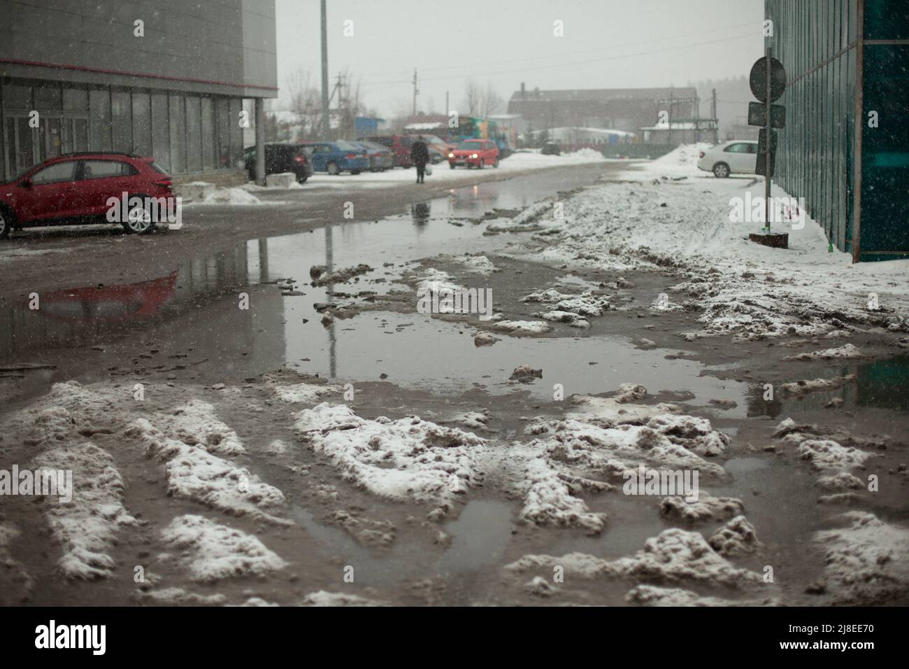 Pozzanghere fangosa di neve sciolta su strada. Parcheggio non pulito. L'asfalto è coperto di neve. Foto Stock