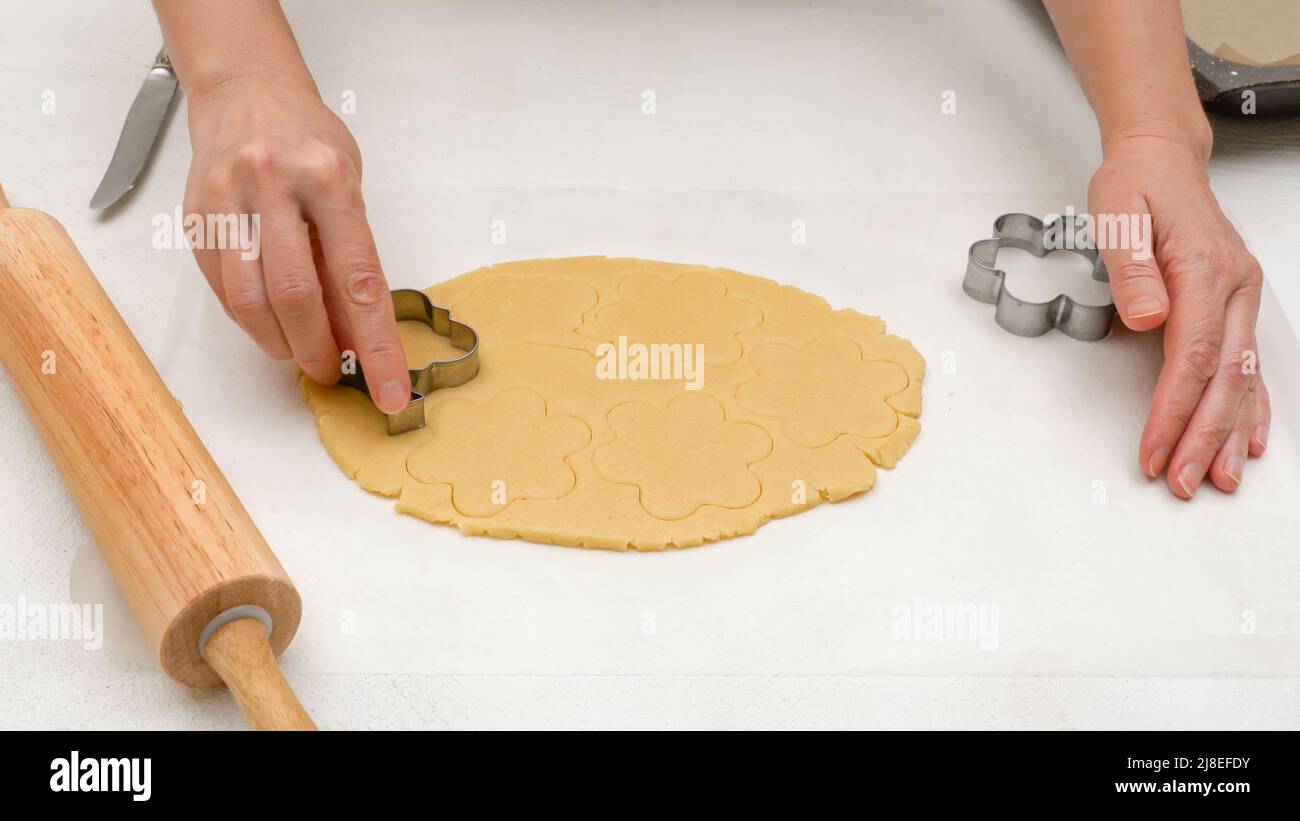 Biscotti impasto primo piano su tavolo da cucina. La donna taglia i biscotti shortbread a forma di fiore, primo piano il processo di cottura Foto Stock