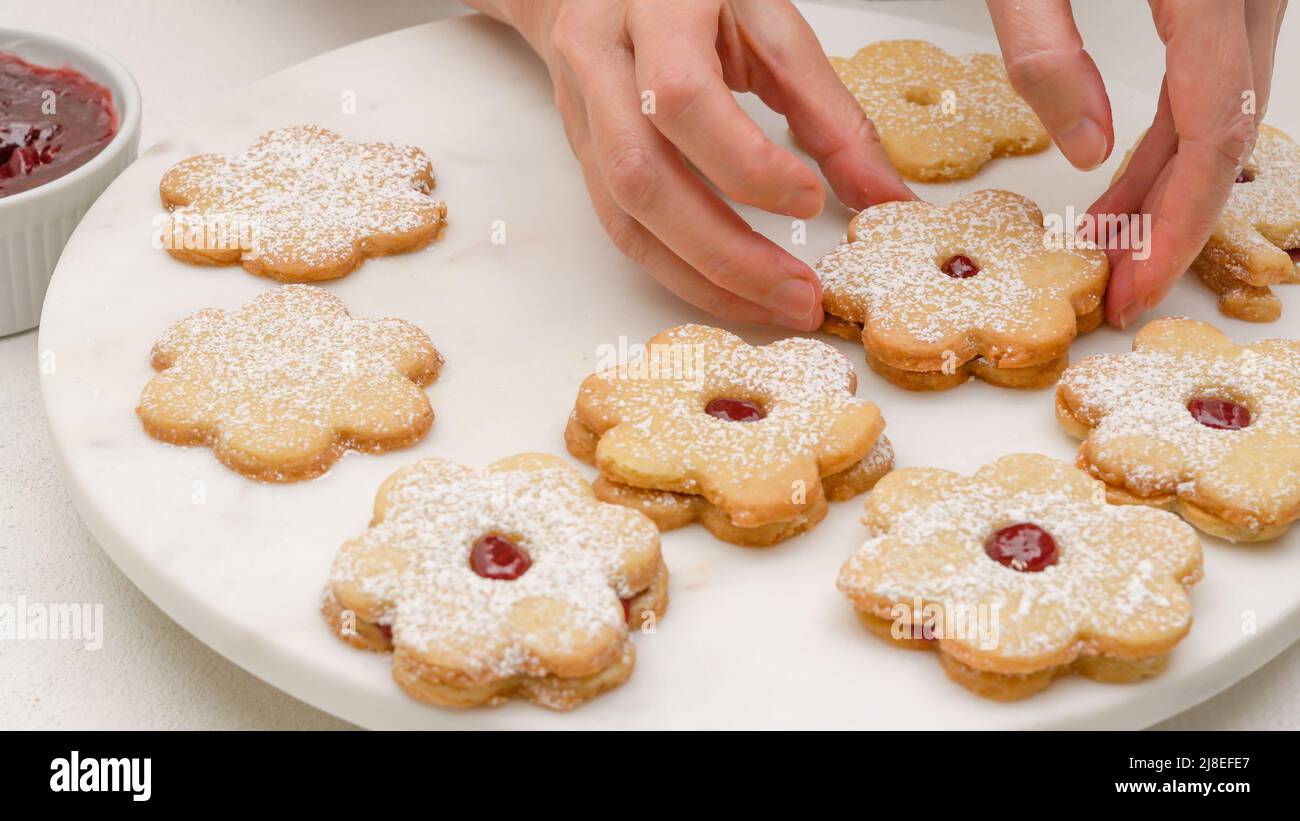 Biscotti frolla a forma di fiore riempiti con ricetta di marmellata di lamponi. Biscotti appena sfornati da vicino su vassoio di marmo Foto Stock