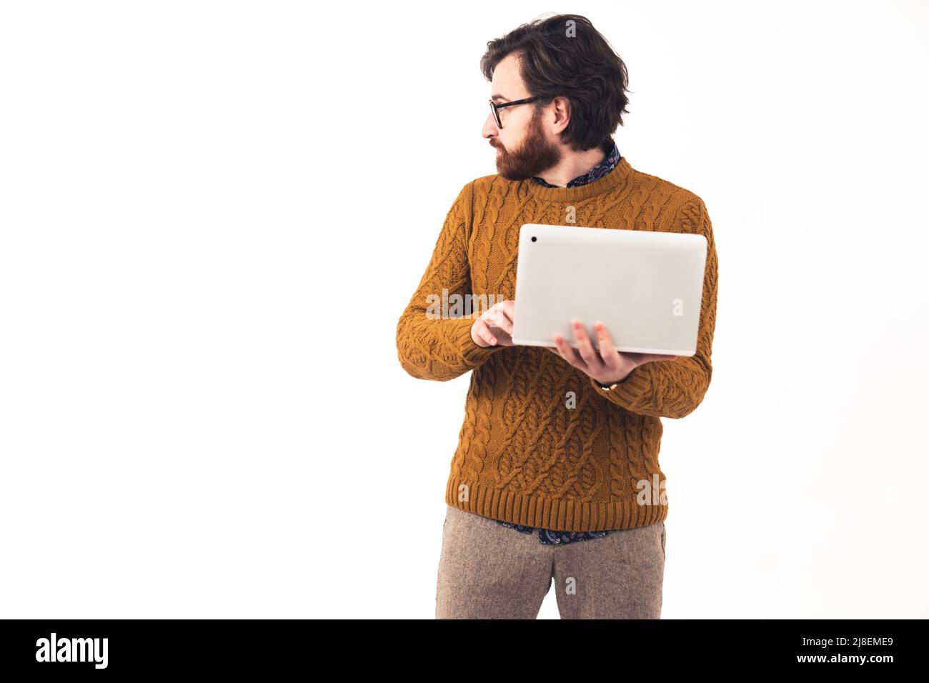 Studio girato su sfondo bianco di un ragazzo sicuro e serio hipster che tiene in mano un moderno notebook guardandolo via vestito con un ponticello di senape. Foto di alta qualità Foto Stock