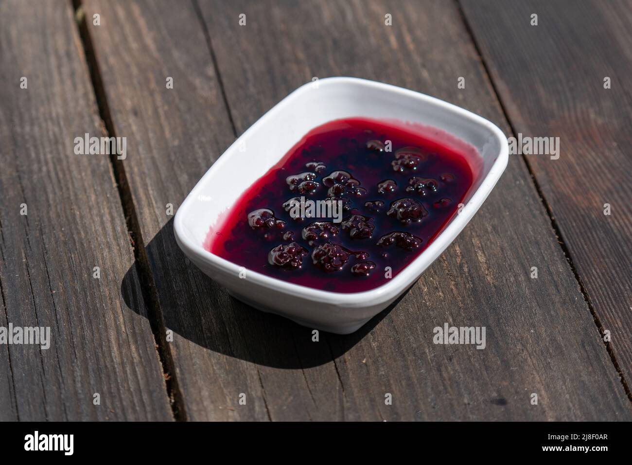 Messa a fuoco selettiva verso il basso della piastra di marmellata di blackberry su tavola di legno. Foto Stock