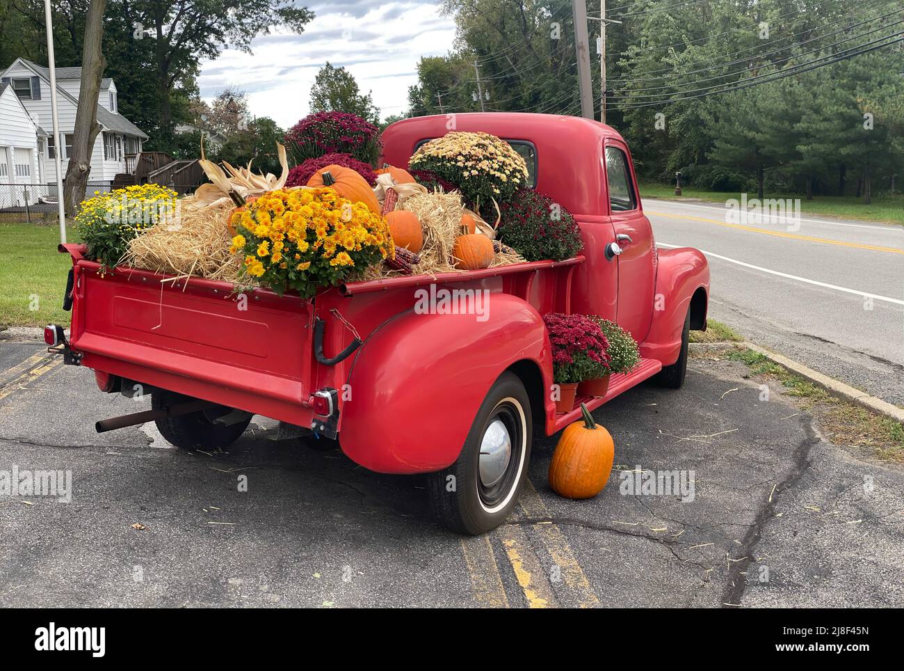Camion di pick up rosso classico con portellone coperto con autunno Halloween fieno decorato stagionale, fiori e zucca arancione Foto Stock