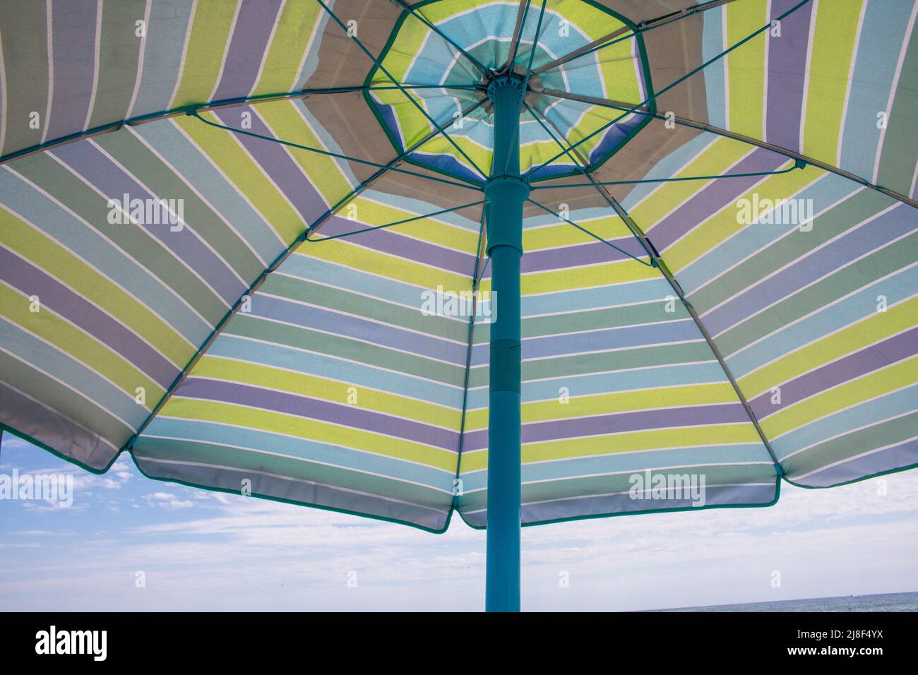 guardando su un'embrella da spiaggia aperta con linee blu, grigie e gialle Foto Stock