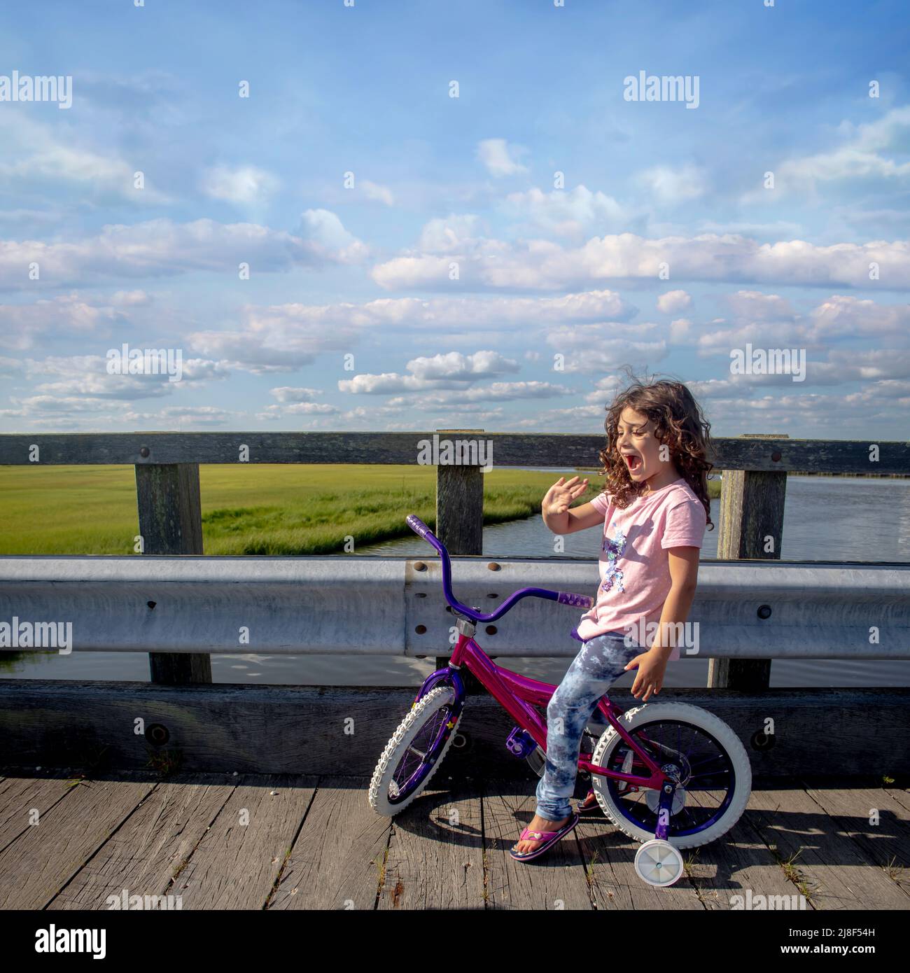 I ragazza bambino seduto su una bicicletta di ruota di allenamento su un ponte di vie d'acqua Foto Stock