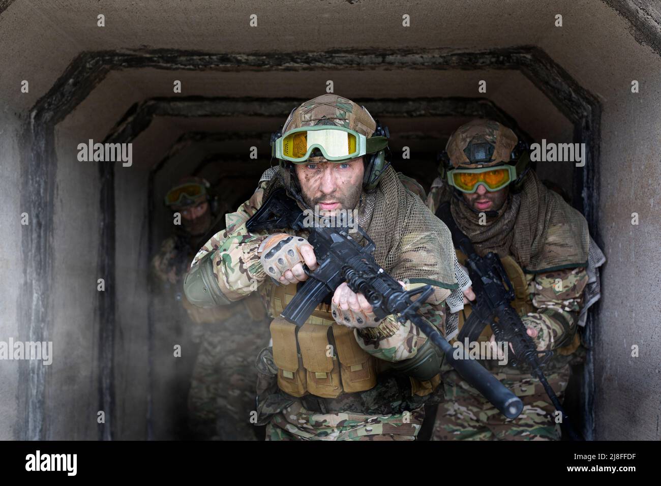 Tre mercenari militari camminano sullo sfondo di un muro di cemento e fumo. Foto con spazio di copia. Collage - un modello in tre pose. Selezionare Foto Stock