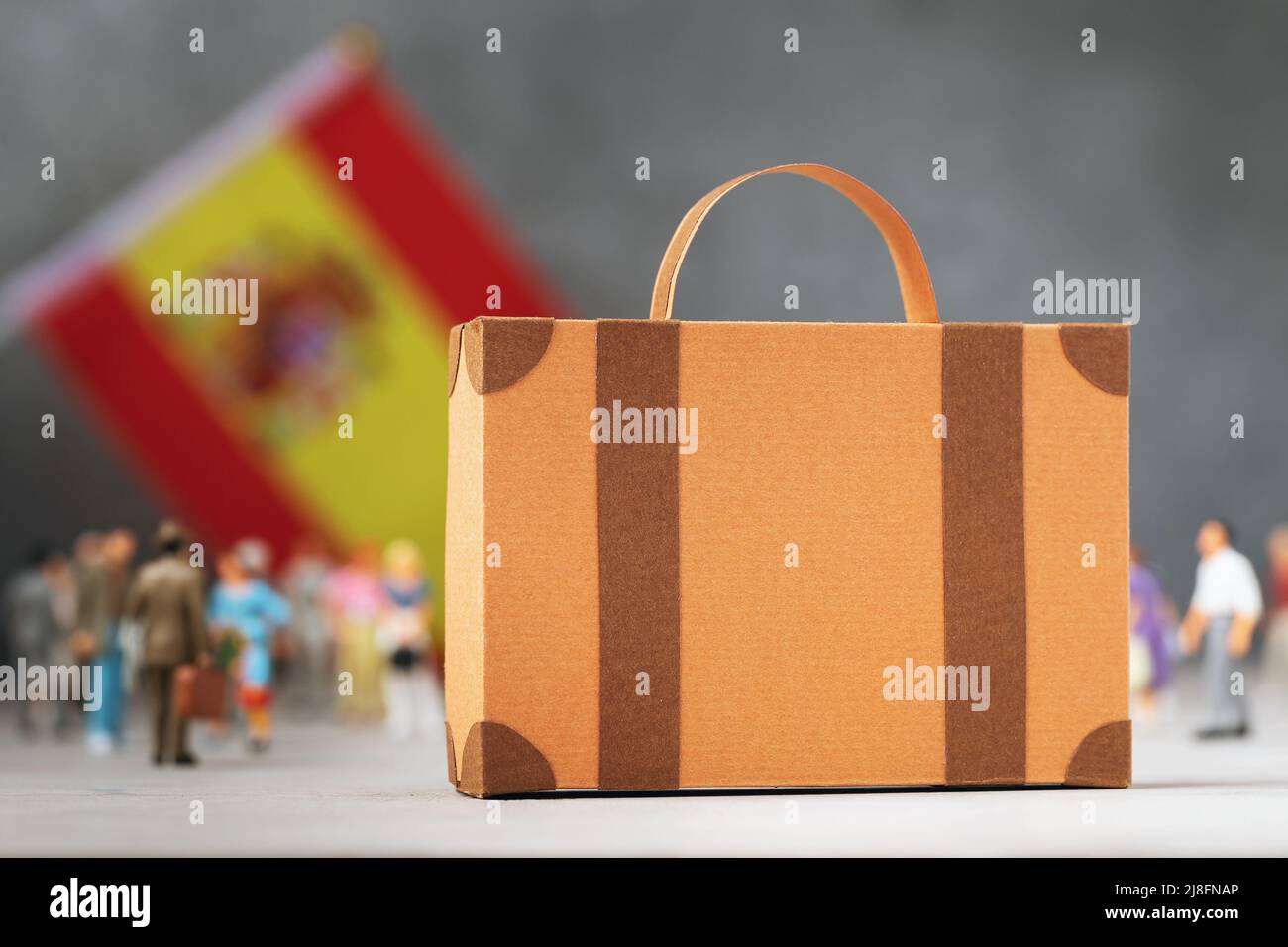 Valigia di cartone, giocattolo di plastica e una bandiera su uno sfondo astratto, un concetto sul tema del trasferimento o migrazione in Spagna Foto Stock