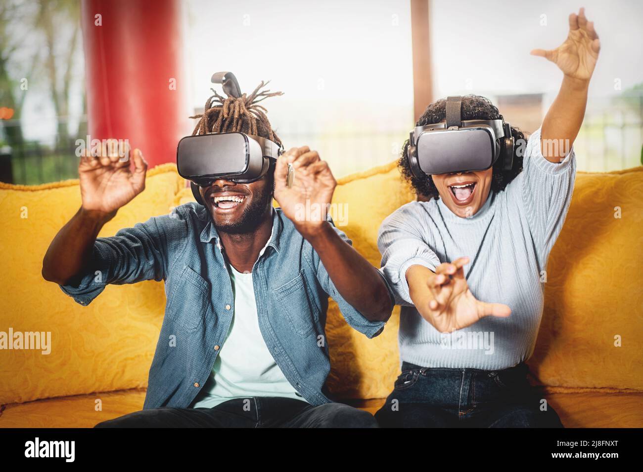 Coppia di amici felici che godono di un gioco virtuale 3D indossando occhiali di realtà virtuale seduto sul divano interno - tecnologia e concetto di stile di vita della gente Foto Stock