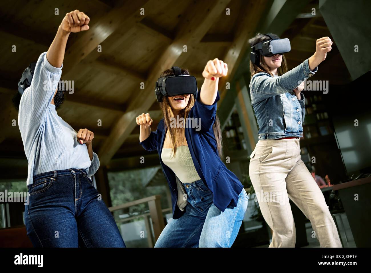Gruppo di giovani donne che usano la cuffia per realtà virtuale - Girlfriends che gioca a ninja combattimento video giochi in meta verse spazio con futuristico occhiali con fu Foto Stock